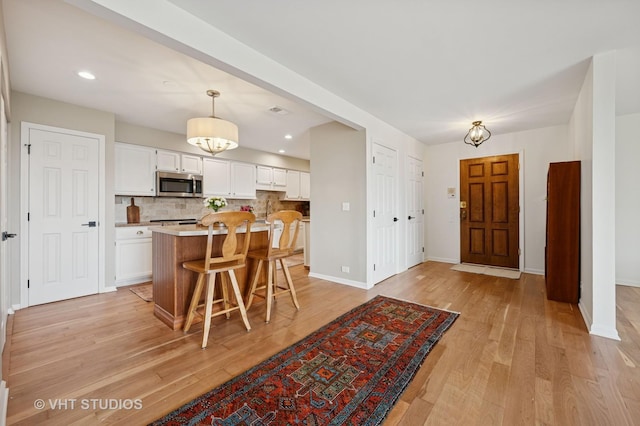 kitchen with stainless steel microwave, white cabinetry, light countertops, backsplash, and recessed lighting