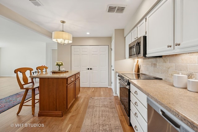 kitchen with appliances with stainless steel finishes, a kitchen breakfast bar, light wood-style floors, backsplash, and white cabinets