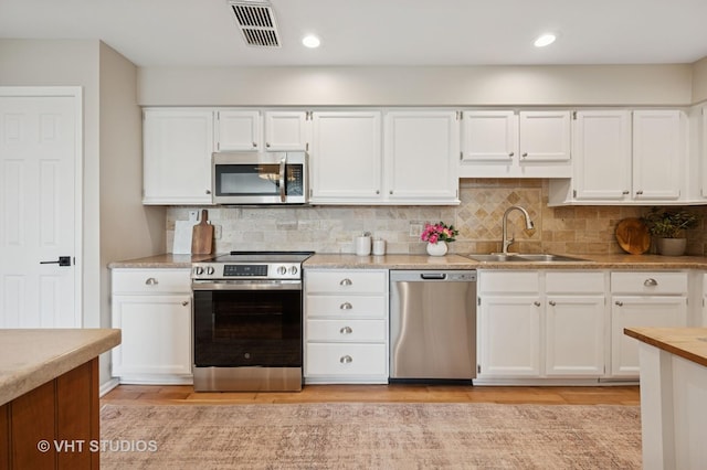 kitchen with stainless steel appliances, a sink, white cabinets, light countertops, and recessed lighting