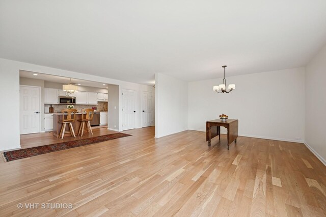 unfurnished living room featuring a chandelier, light wood-type flooring, baseboards, and recessed lighting