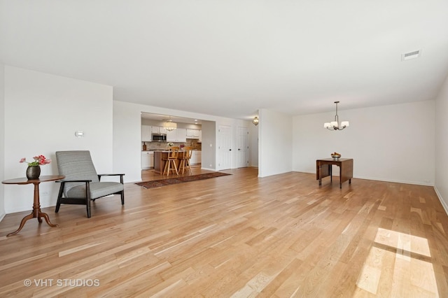 living room featuring light wood-type flooring, a chandelier, and baseboards