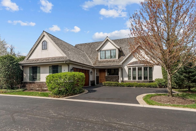 view of front facade with an attached garage, stucco siding, stone siding, and driveway