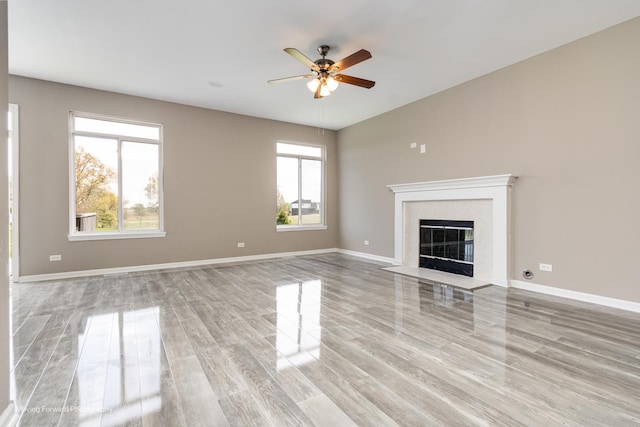 unfurnished living room featuring light wood-style floors, a ceiling fan, baseboards, and a tile fireplace