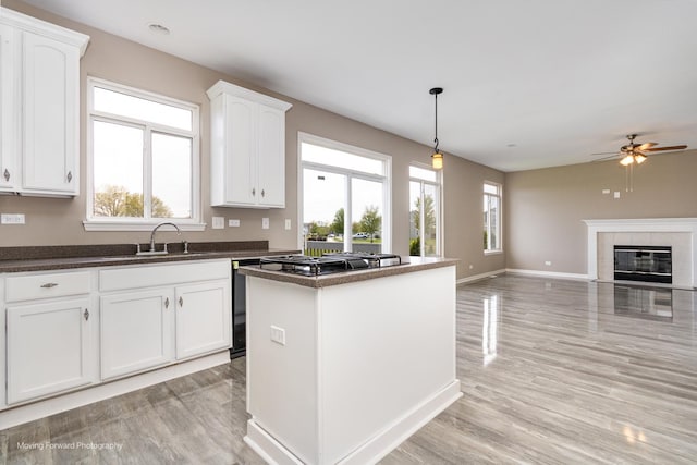 kitchen featuring a ceiling fan, a kitchen island, a sink, white cabinets, and light wood-style flooring