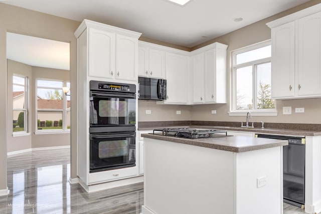 kitchen with a center island, a sink, baseboards, black appliances, and white cabinetry