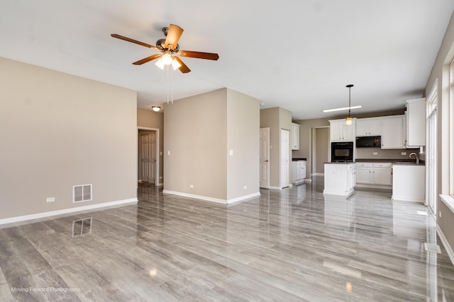 unfurnished living room featuring baseboards, a ceiling fan, light wood-type flooring, and visible vents