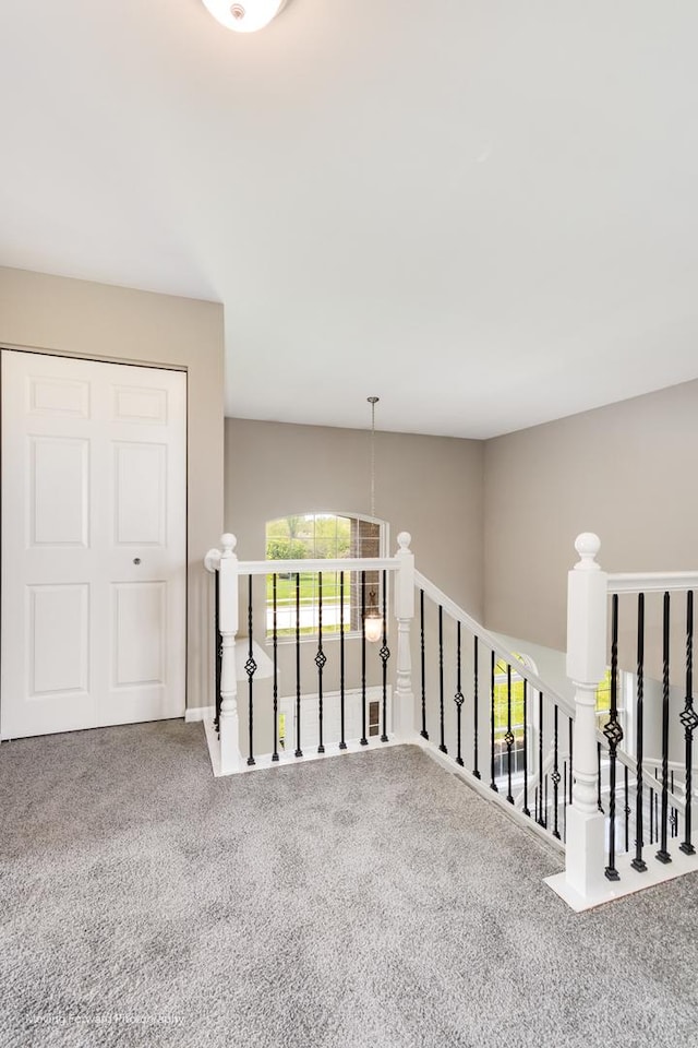 hall with carpet floors, an upstairs landing, and a healthy amount of sunlight