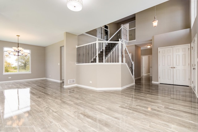 unfurnished living room featuring visible vents, stairs, wood finished floors, baseboards, and a notable chandelier