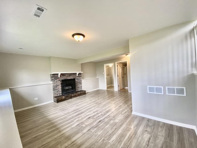 unfurnished living room featuring baseboards, wood finished floors, and a brick fireplace