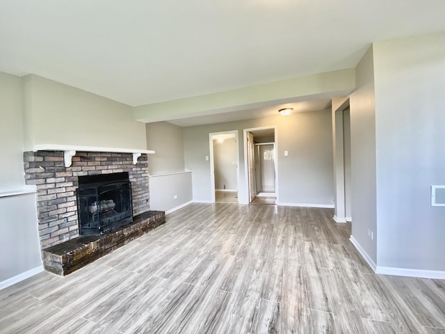 unfurnished living room with wood finished floors, baseboards, and a brick fireplace
