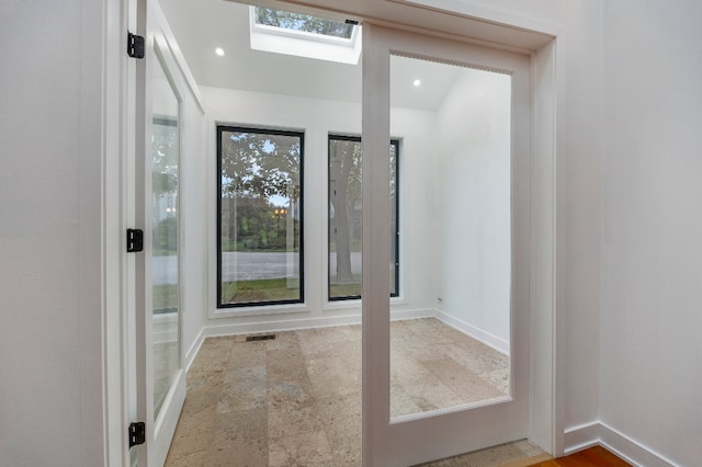 doorway featuring plenty of natural light, stone finish flooring, baseboards, and a skylight