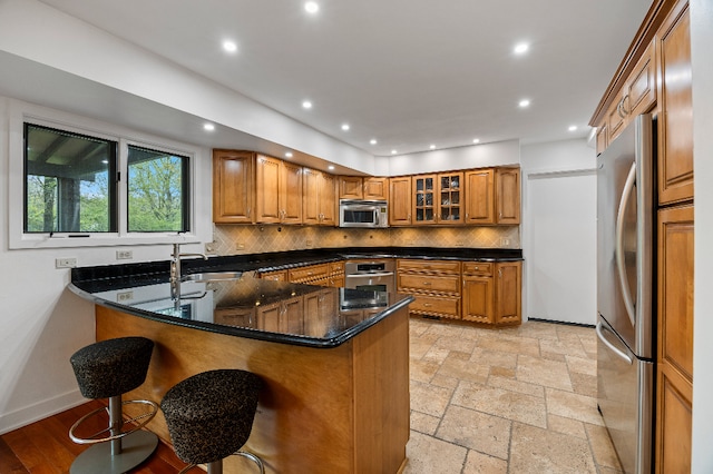 kitchen featuring a peninsula, brown cabinets, tasteful backsplash, a sink, and appliances with stainless steel finishes