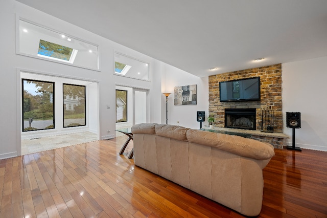 living area featuring a stone fireplace, baseboards, a towering ceiling, and wood finished floors
