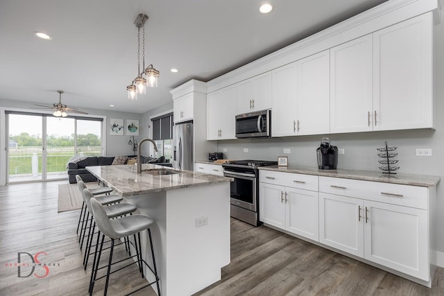 kitchen with a sink, a breakfast bar, recessed lighting, light wood-style flooring, and appliances with stainless steel finishes