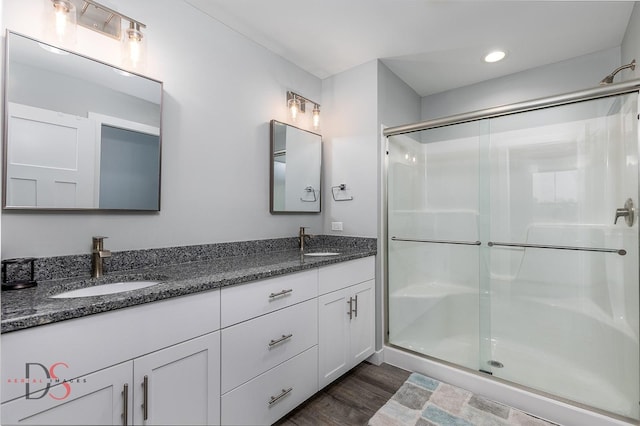 full bathroom with a stall shower, double vanity, a sink, and wood finished floors