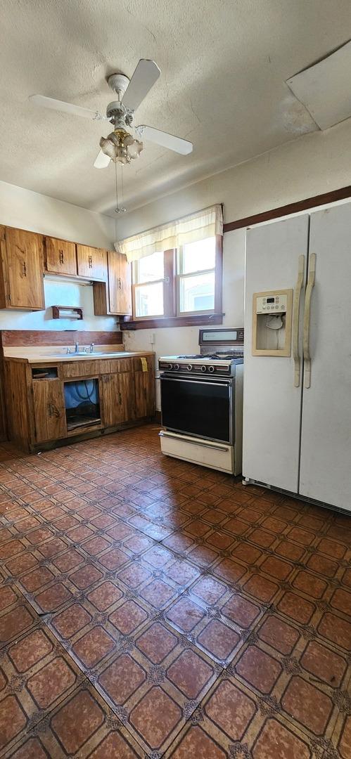 7943 S Vernon Ave, Chicago, IL 60619 - kitchen with electric range oven, white refrigerator with ice dispenser, brown cabinetry, a textured ceiling, and a ceiling fan
