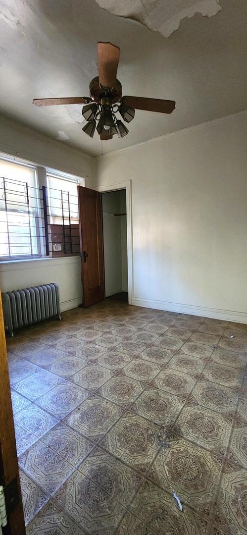 7943 S Vernon Ave, Chicago, IL 60619 - unfurnished bedroom with radiator heating unit, a closet, a ceiling fan, and baseboards