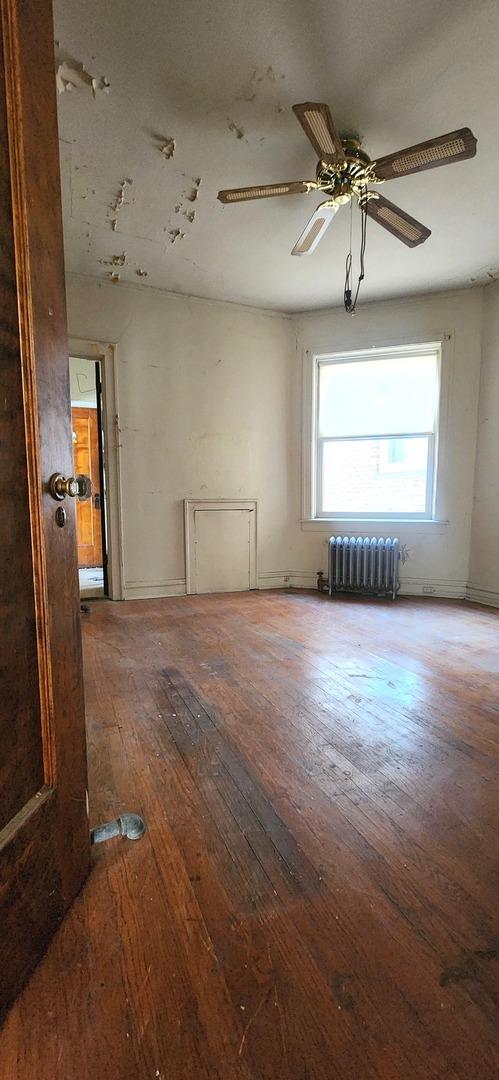 7943 S Vernon Ave, Chicago, IL 60619 - unfurnished room with radiator heating unit, wood-type flooring, and ceiling fan
