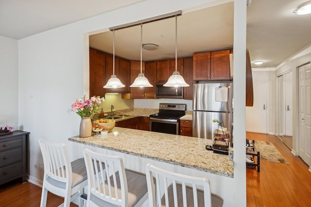 kitchen featuring a sink, brown cabinets, wood finished floors, light stone countertops, and appliances with stainless steel finishes