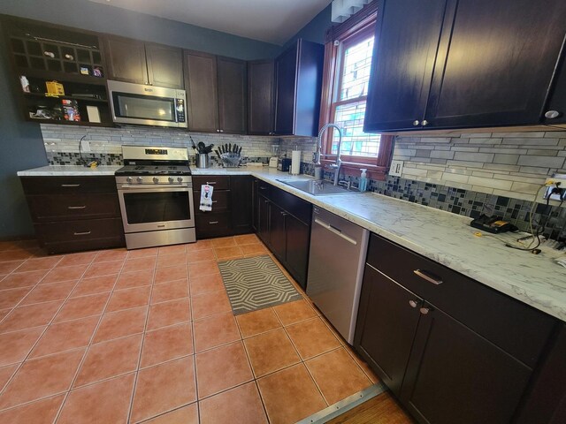 kitchen with light tile patterned floors, a sink, backsplash, light countertops, and appliances with stainless steel finishes