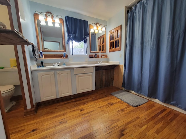 full bath featuring a sink, toilet, a chandelier, wood-type flooring, and double vanity