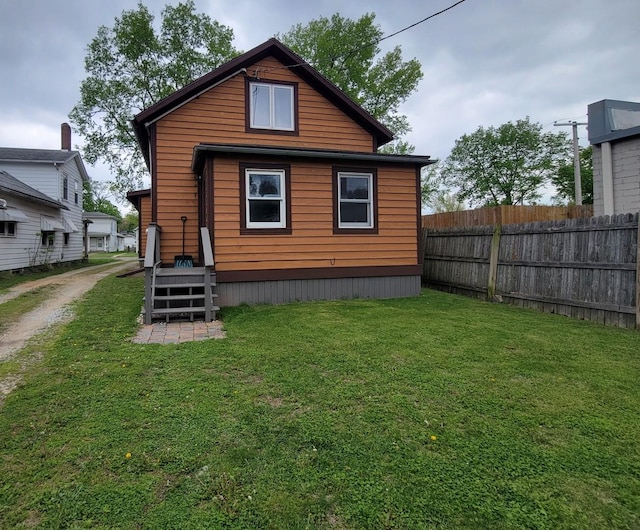 back of house featuring dirt driveway, fence, and a lawn