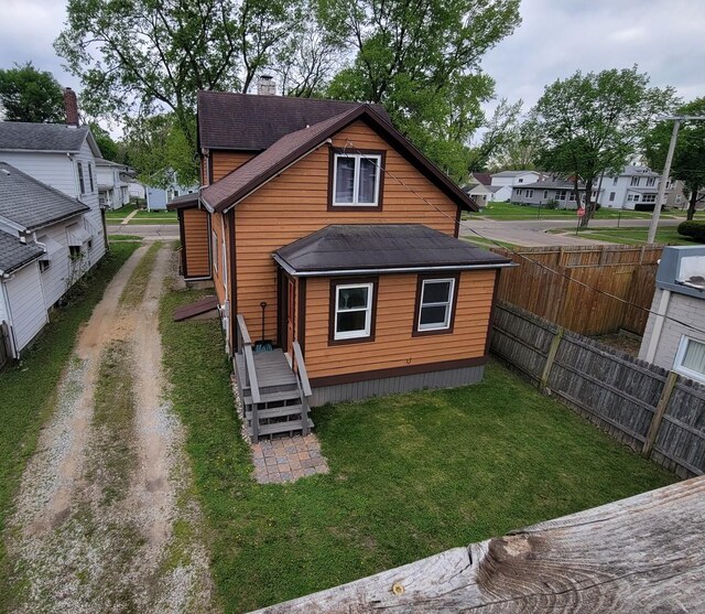 back of property with a chimney, a lawn, fence, dirt driveway, and a residential view
