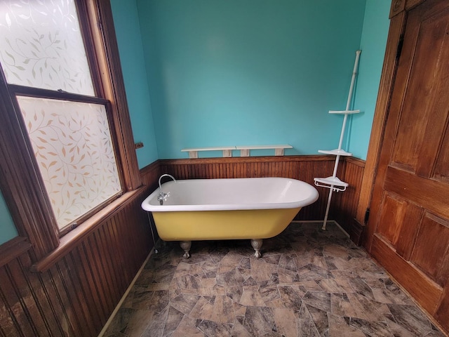 full bathroom featuring a freestanding bath, wood walls, wainscoting, and stone finish floor