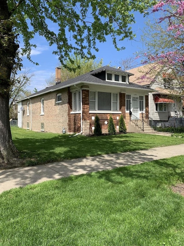 bungalow-style home with brick siding, a front lawn, and a chimney