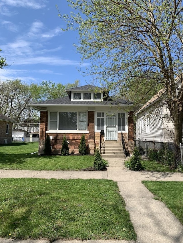 bungalow-style house with a front lawn, a shingled roof, brick siding, and fence