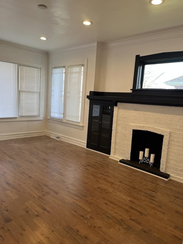 unfurnished living room with wood finished floors, visible vents, a fireplace, and ornamental molding