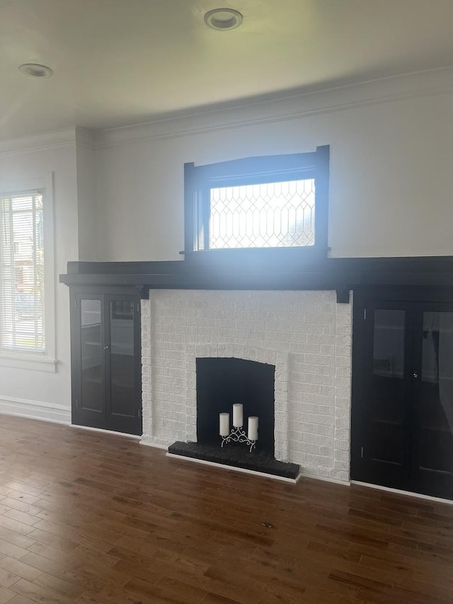 unfurnished living room with ornamental molding, a brick fireplace, plenty of natural light, and wood finished floors