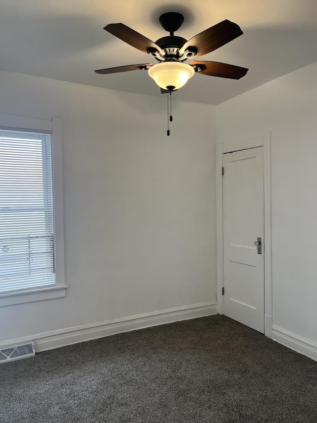 spare room featuring baseboards, a ceiling fan, visible vents, and dark carpet