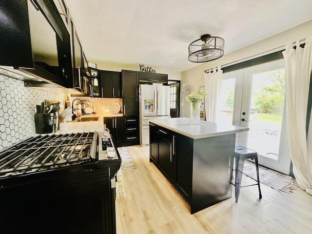 1310 E 15th Rd, Streator, IL 61364 - kitchen with white fridge with ice dispenser, dark cabinetry, gas range oven, decorative backsplash, and light wood-style floors