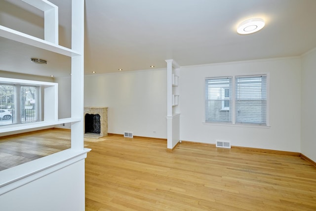 unfurnished living room with baseboards, a high end fireplace, visible vents, and wood finished floors