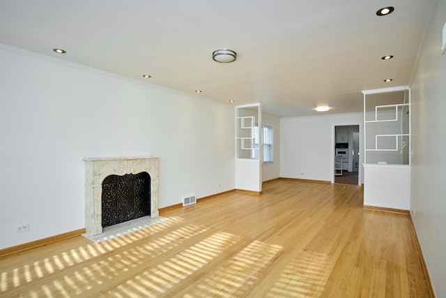 unfurnished living room featuring ornamental molding, light wood finished floors, a high end fireplace, and visible vents