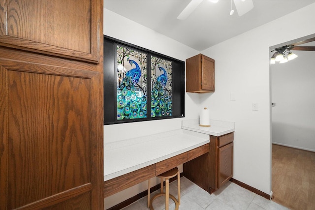 unfurnished office featuring built in desk, baseboards, and ceiling fan