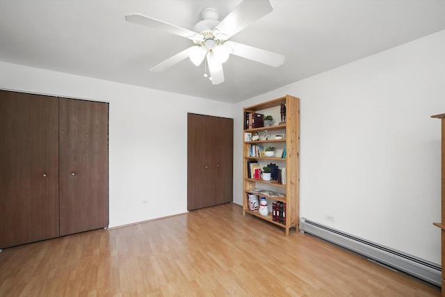 unfurnished bedroom with light wood finished floors, a ceiling fan, multiple closets, and a baseboard heating unit
