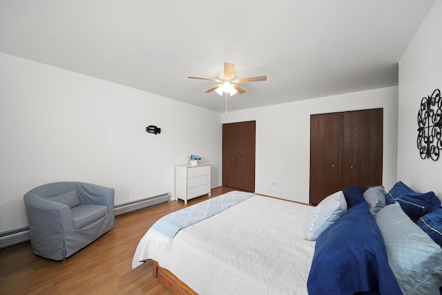 bedroom featuring a ceiling fan, wood finished floors, baseboard heating, and multiple closets