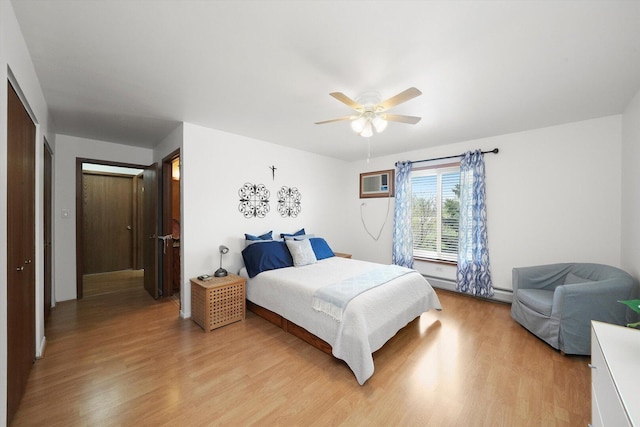 bedroom with light wood finished floors, an AC wall unit, ceiling fan, and a baseboard heating unit