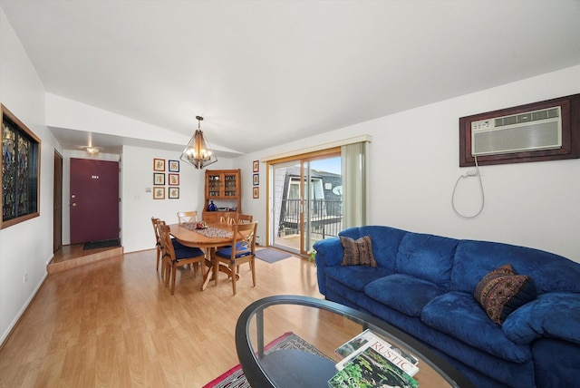 living area featuring light wood finished floors, an inviting chandelier, vaulted ceiling, and an AC wall unit