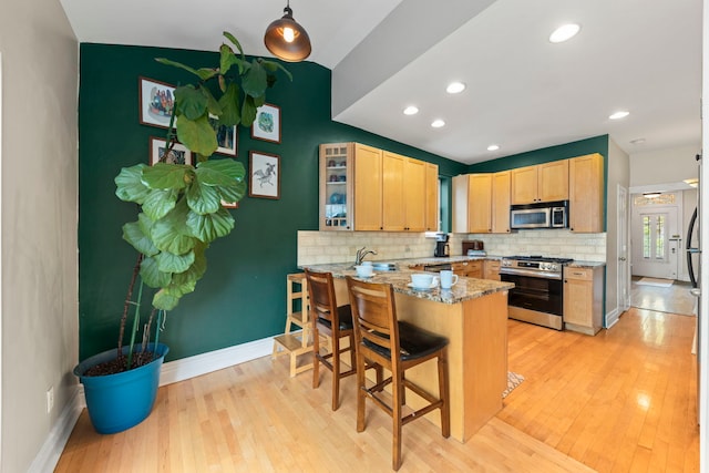 kitchen featuring appliances with stainless steel finishes, light brown cabinets, backsplash, a peninsula, and light wood-type flooring