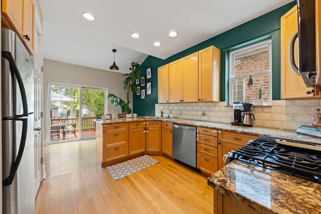 kitchen with appliances with stainless steel finishes, a peninsula, backsplash, light wood finished floors, and light stone countertops