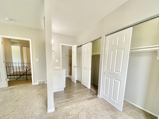 unfurnished bedroom with multiple closets, light carpet, and baseboards