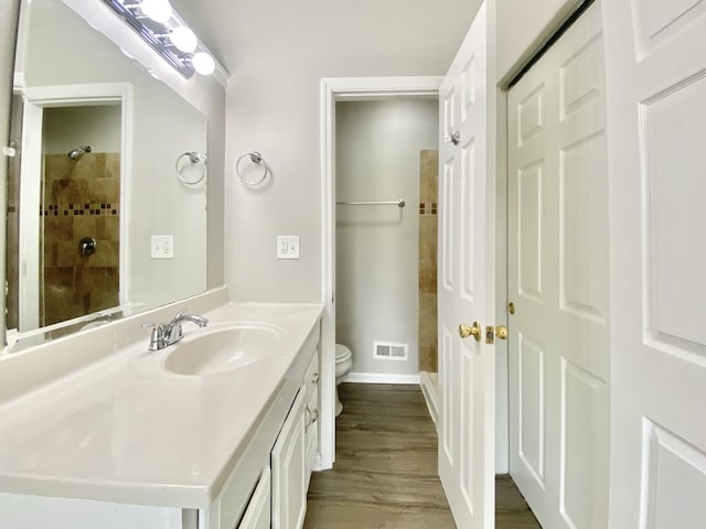 bathroom featuring toilet, a tile shower, vanity, wood finished floors, and baseboards
