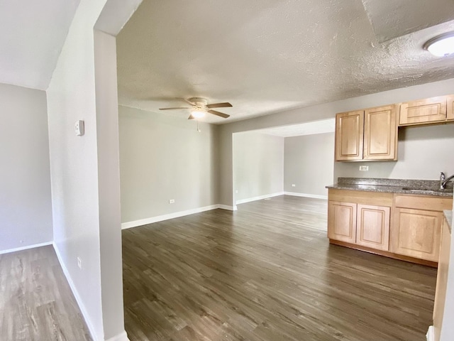 kitchen with light brown cabinetry, a sink, dark wood-type flooring, a ceiling fan, and baseboards