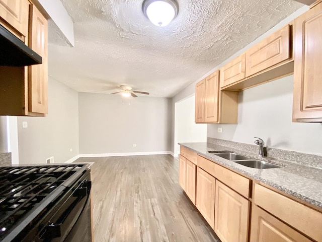 kitchen featuring light brown cabinetry, a sink, light wood finished floors, a ceiling fan, and black range with gas cooktop