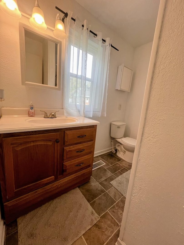 bathroom with toilet, baseboards, a textured wall, and vanity