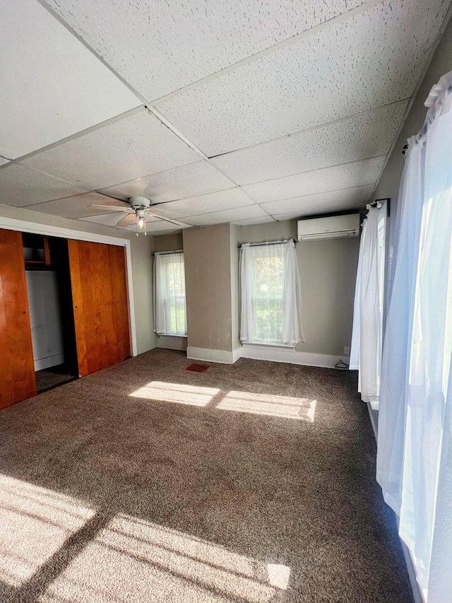 unfurnished room featuring carpet floors, an AC wall unit, baseboards, and a paneled ceiling