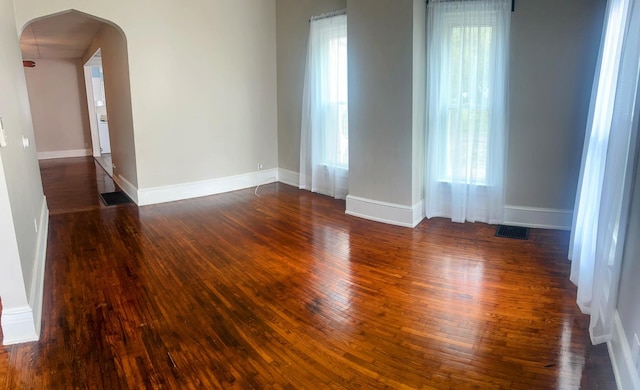 unfurnished room with arched walkways, baseboards, dark wood-style floors, and visible vents